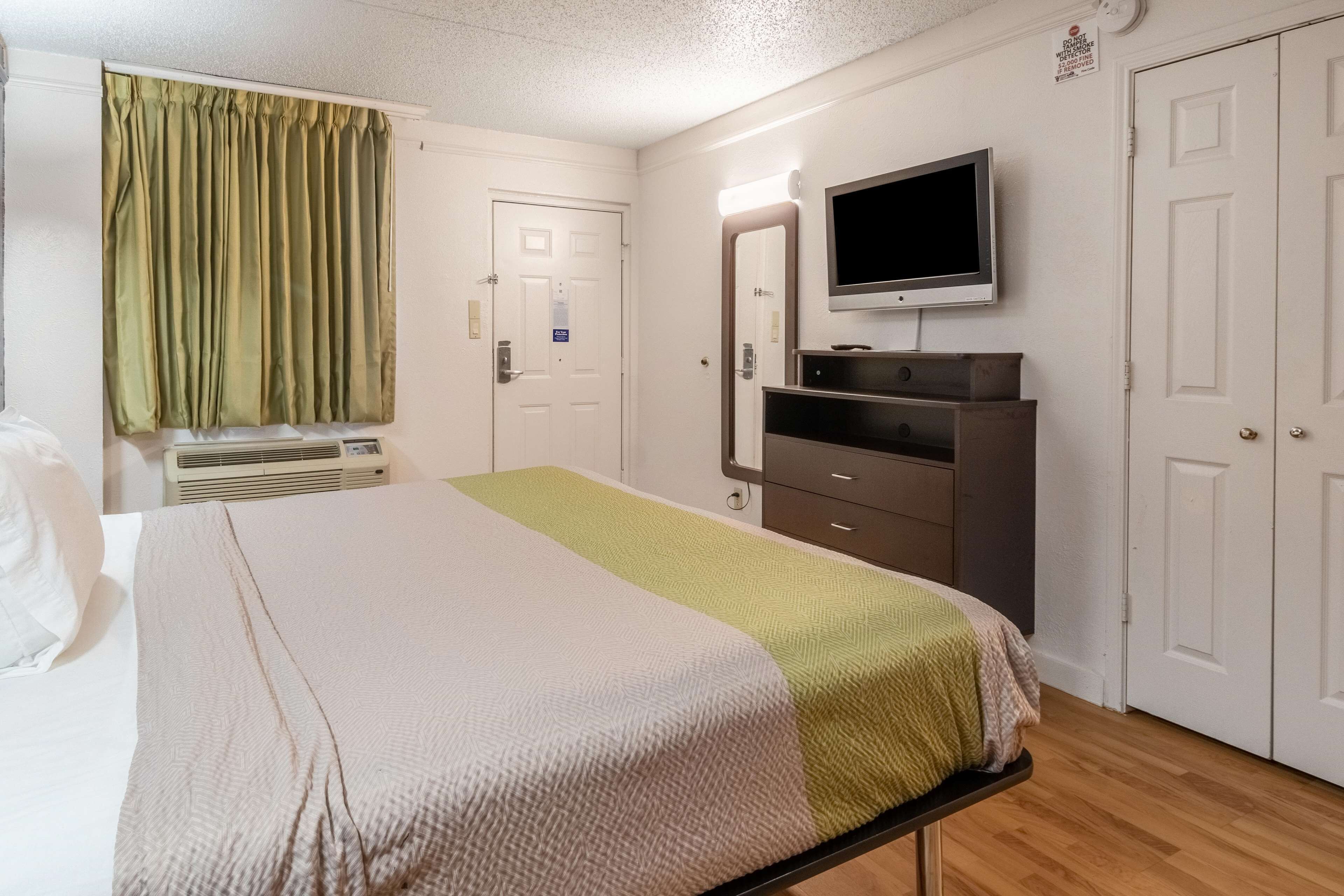 A hotel room with a bed, a television mounted on the wall, a dresser, and a door.