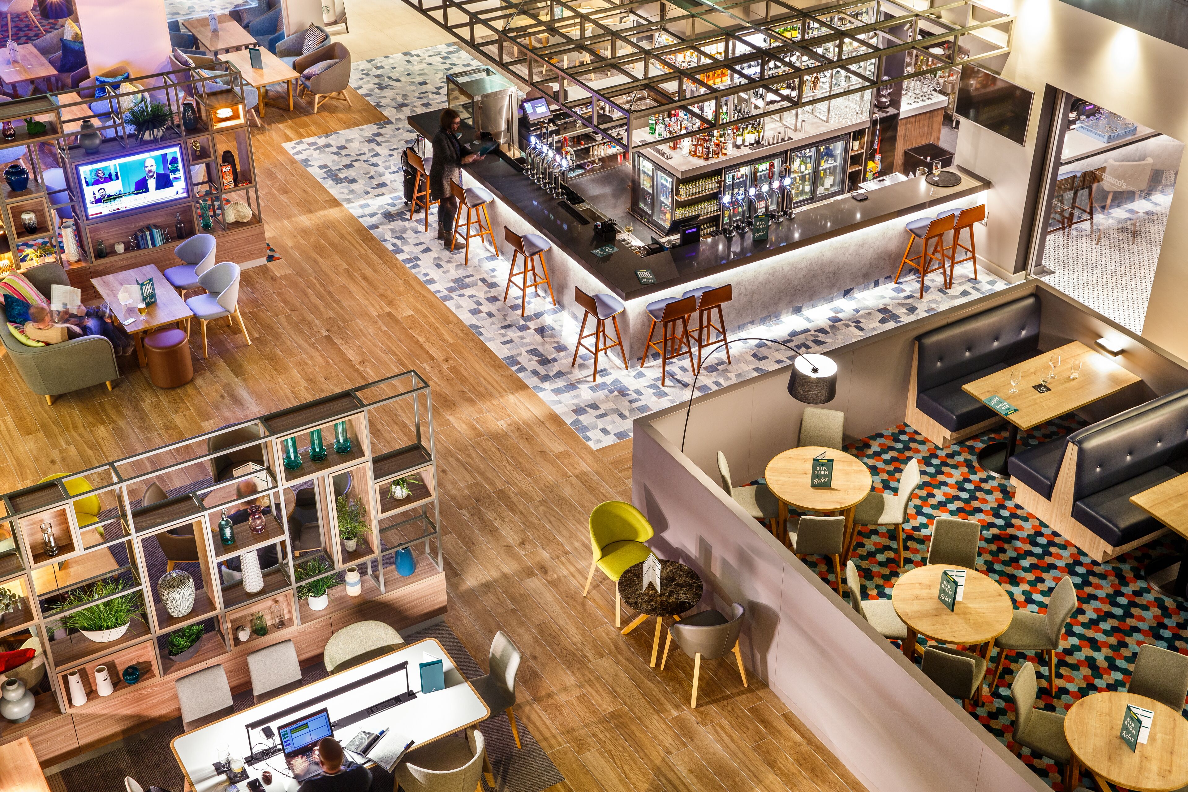 A modern bar area with a long counter, stools, and a seating area with tables and chairs.