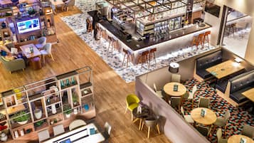 A modern bar area with a long counter, stools, and a seating area with tables and chairs.
