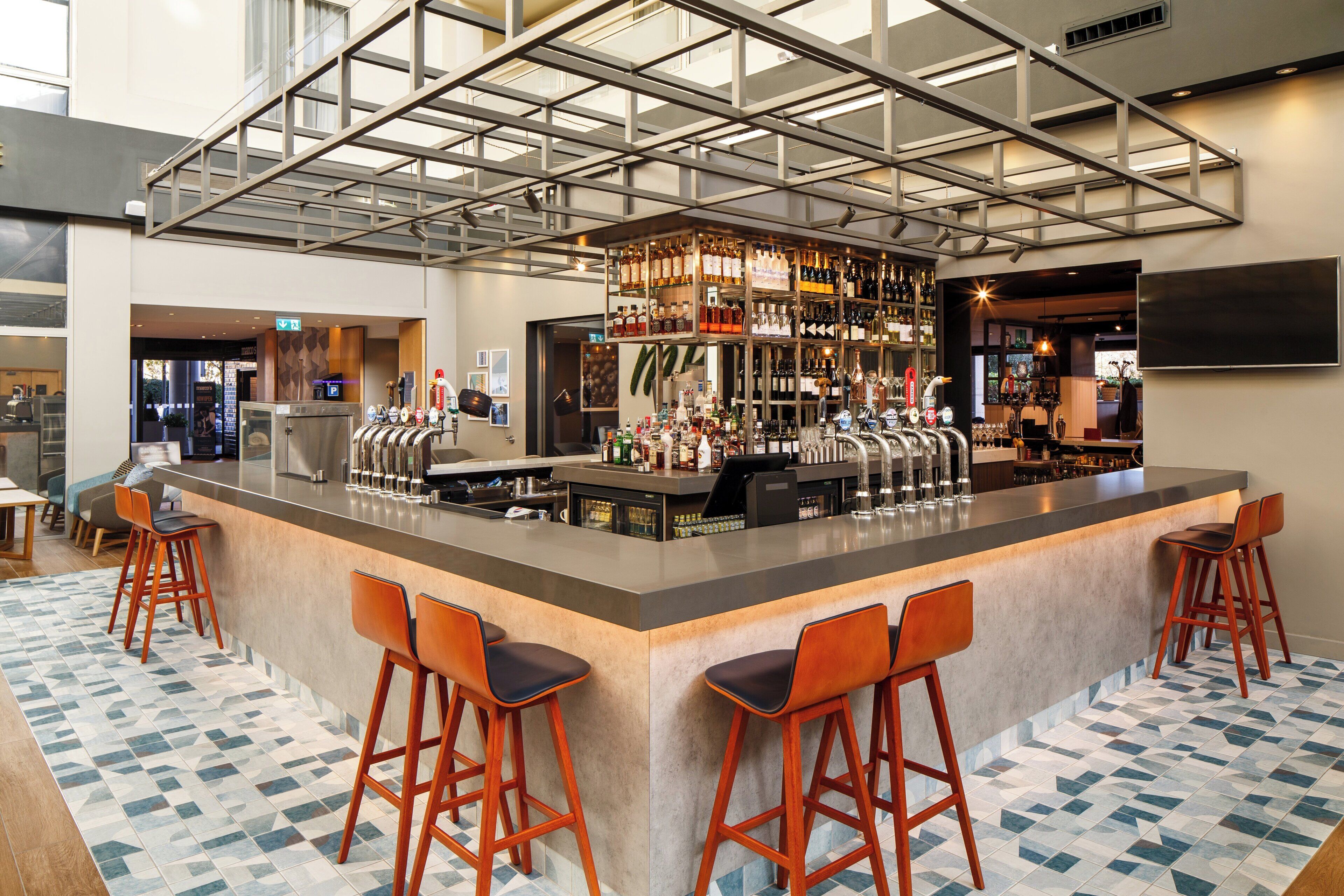 A bar area with a bar counter, stools, and a variety of bottles and glasses.