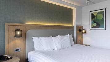 A hotel room with a large bed, a bedside table with a lamp, and a wall-mounted light fixture.