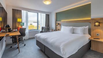 Een moderne hotelkamer met een groot bed, een bureau met stoel, een klein tafeltje met telefoon en een raam met gordijnen.