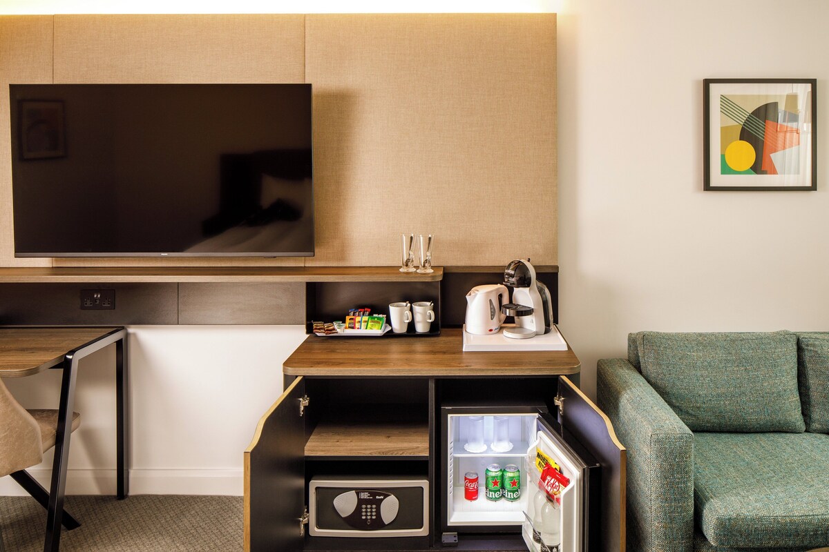 A compact hotel room with a flat-screen TV, a kitchenette with a fridge, a microwave, and a small coffee maker.