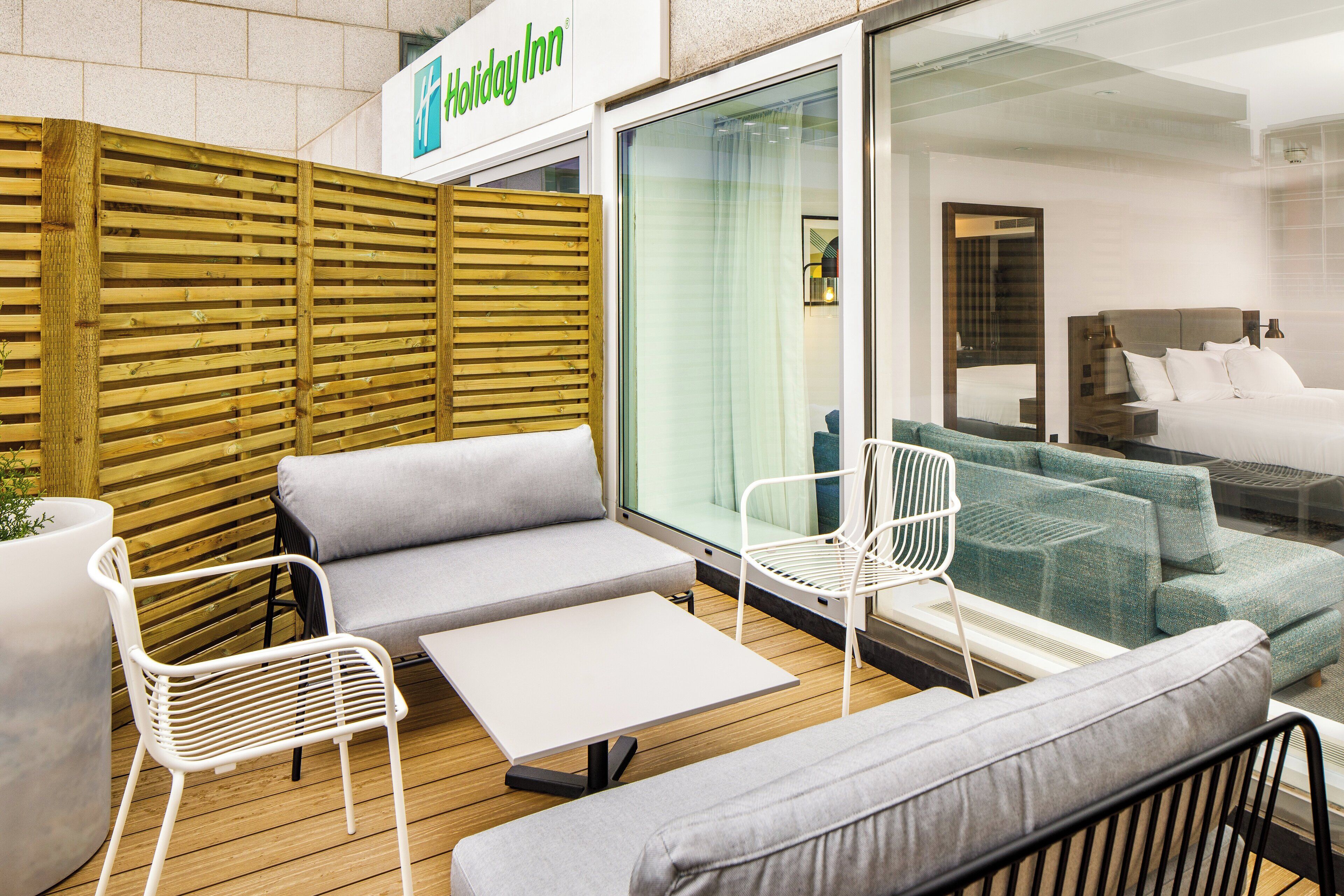 A Holiday Inn room with a wooden partition, grey sofa, white chair, and a bed with a headboard.