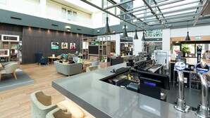 A modern hotel lobby with a bar area, seating, and a large windowed atrium. - Holiday Inn Milton Keynes - Central by IHG (Milton Keynes)