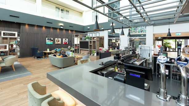 A modern hotel lobby with a bar area, seating, and a large windowed atrium. - Holiday Inn Milton Keynes - Central by IHG (Milton Keynes)