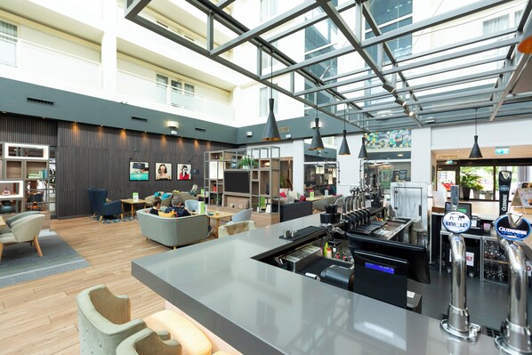 A modern hotel lobby with a bar area, seating, and a large windowed atrium. - Holiday Inn Milton Keynes - Central by IHG (Milton Keynes)