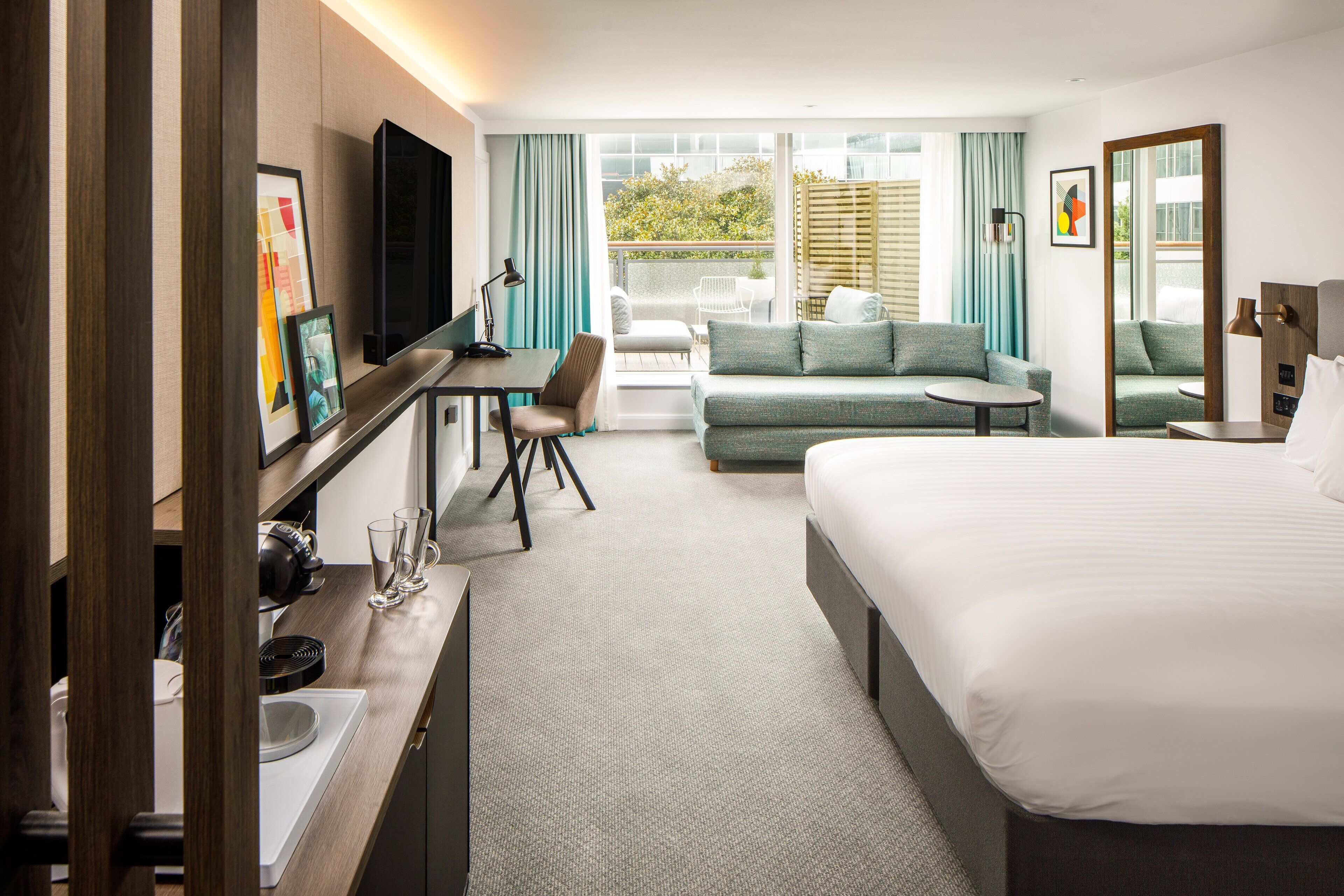 Ein Hotelzimmer mit Bett, Schreibtisch, Sofa und einem Balkon mit Aussicht.