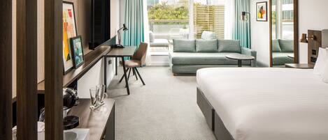 Habitación de hotel con cama, escritorio, sofá y balcón con vistas.