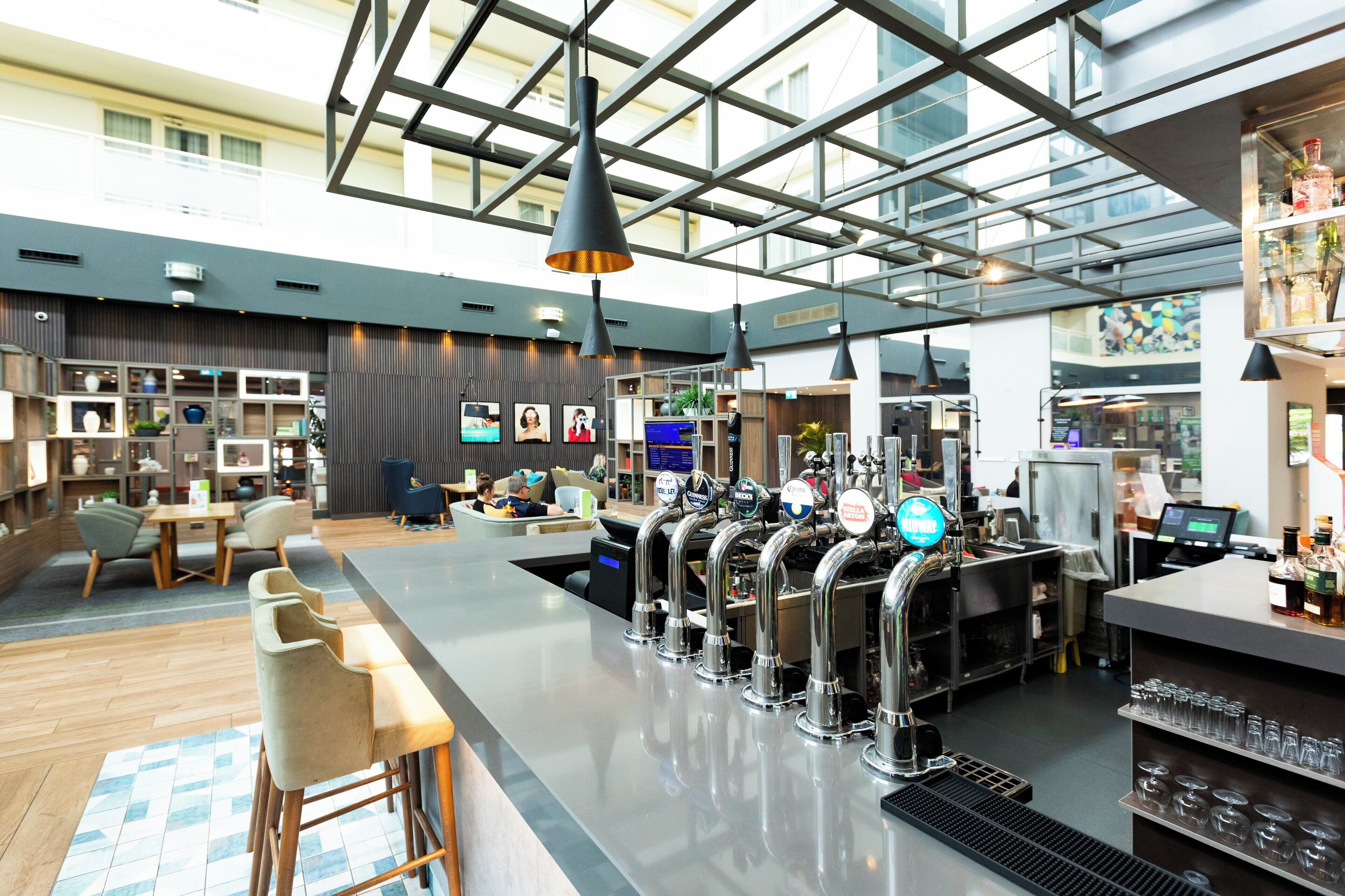 A modern bar area with multiple taps, seating, and a high ceiling with skylights.