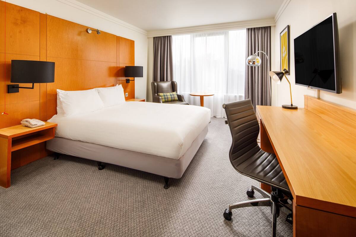 A hotel room with a large bed, a desk, a chair, a TV, and a telephone.