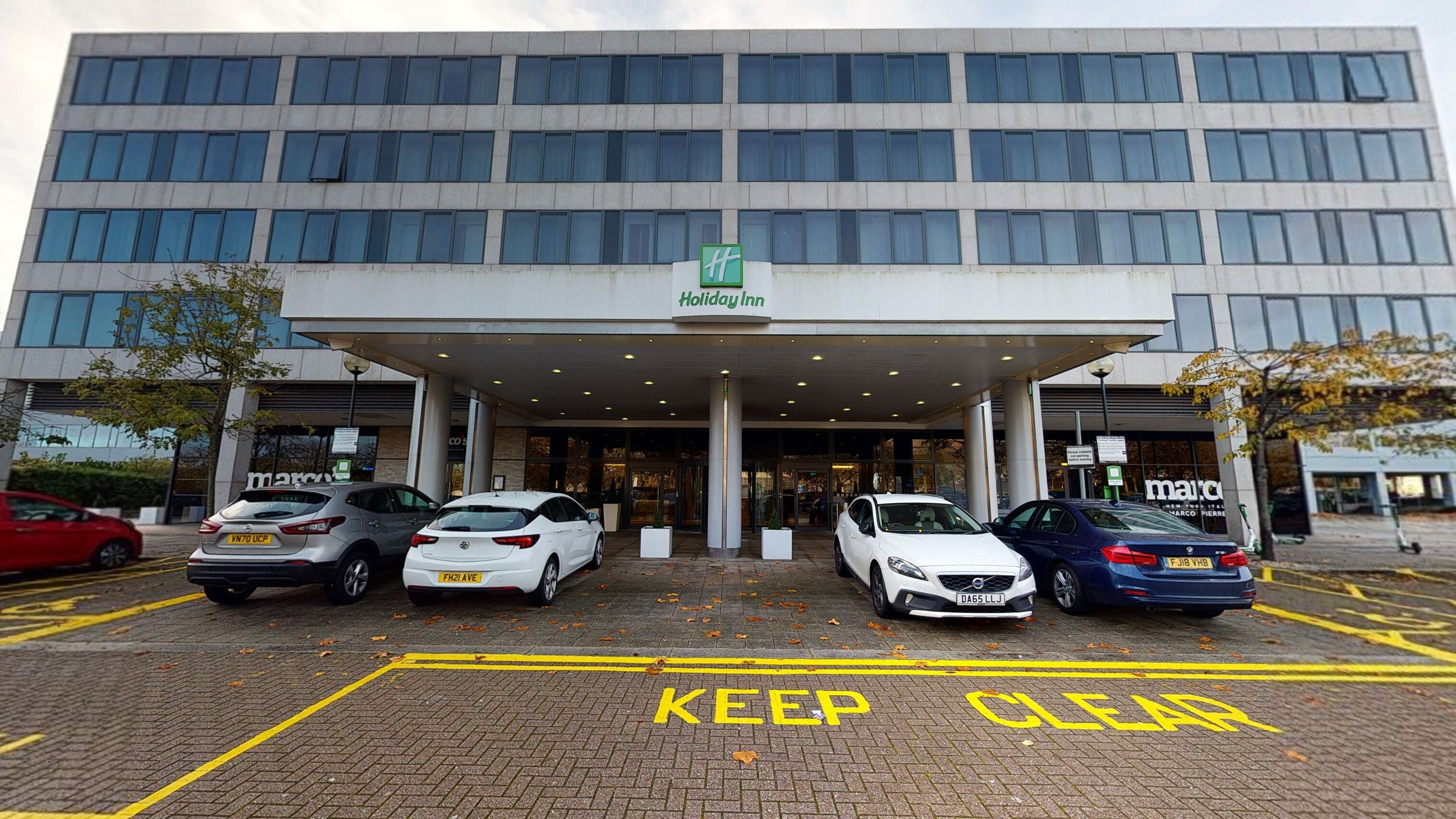 A Holiday Inn hotel with a modern facade, a covered entrance, and a parking lot with cars.