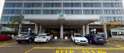 A Holiday Inn hotel with a modern facade, a covered entrance, and a parking lot with cars.