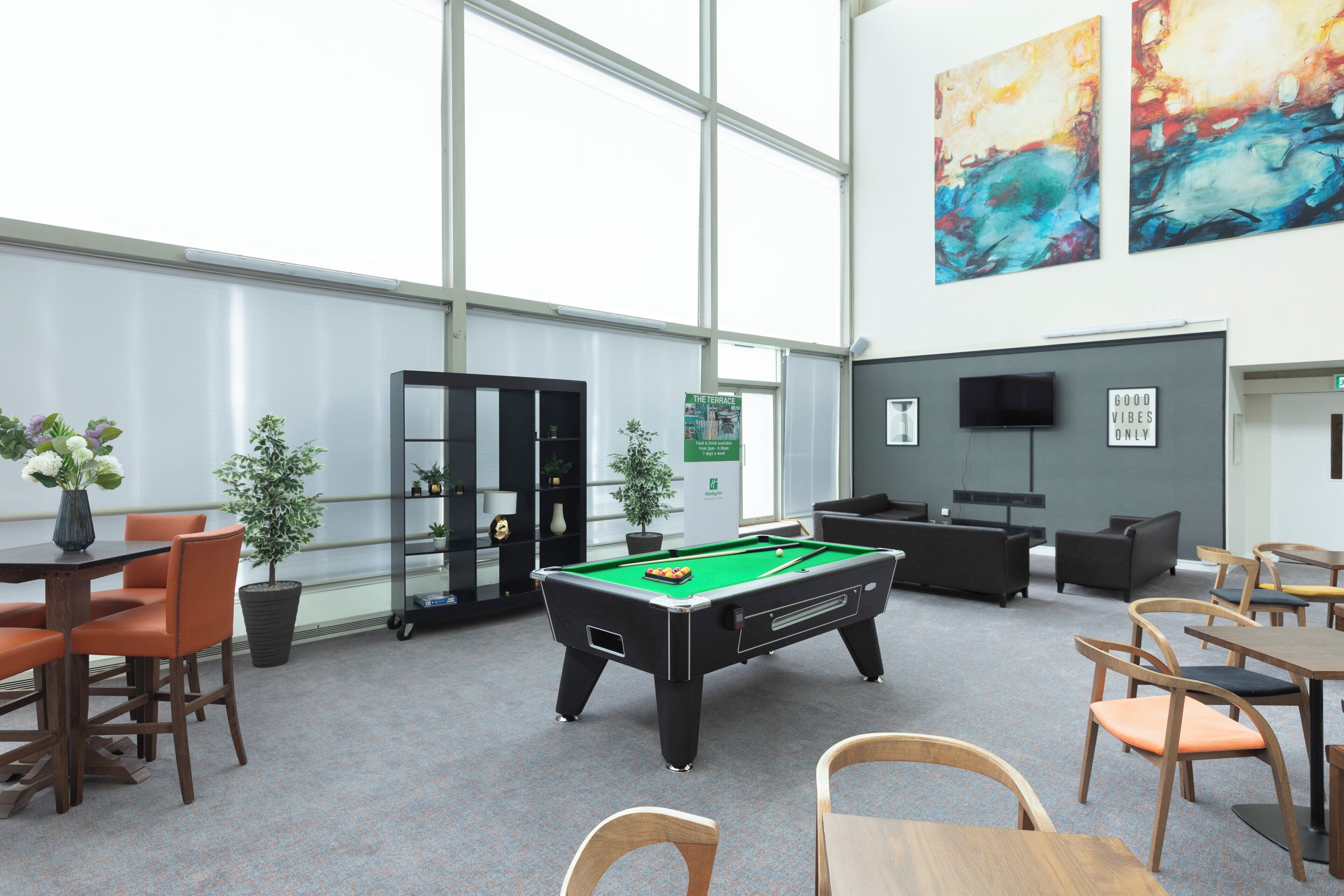 A pool table in a room with large windows, a television, and various seating arrangements.