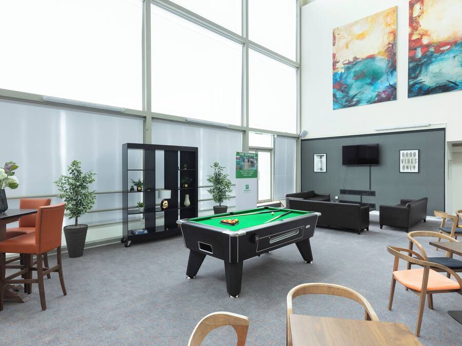 A pool table in a room with large windows, a television, and various seating arrangements.