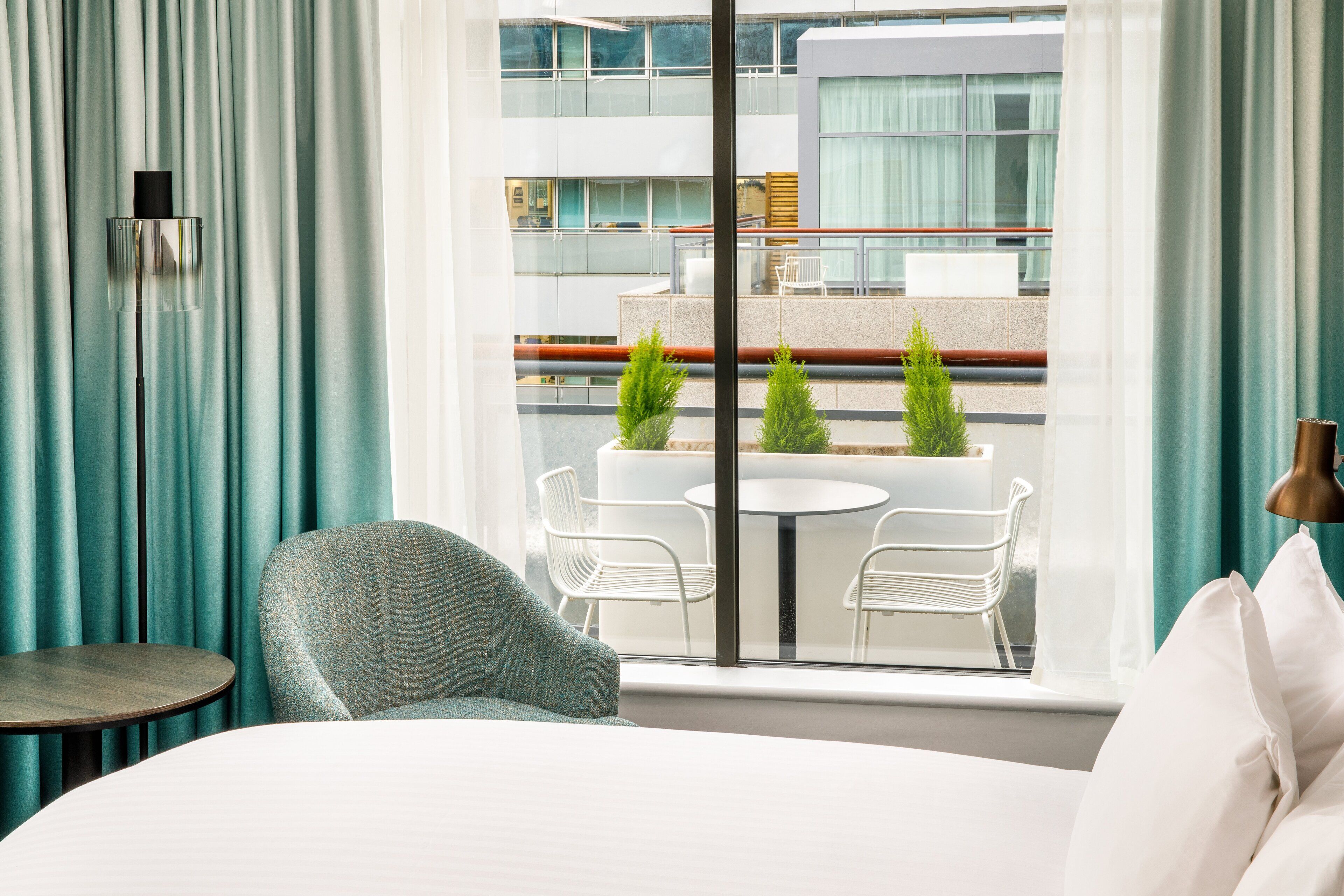 Habitación de hotel con cama, una mesa redonda, dos sillas y vistas a un balcón con mesa y sillas.