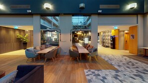 A modern hotel lobby with a central seating area, a reception desk, and a parking area.