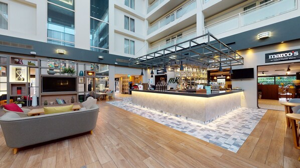 A spacious lobby with a central bar area, seating arrangements, and a high ceiling with natural light. - Holiday Inn Milton Keynes - Central by IHG (Milton Keynes)