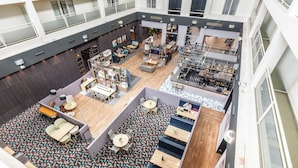 A spacious indoor area with multiple seating arrangements, a central open space, and a mezzanine level with a railing. - Holiday Inn Milton Keynes - Central by IHG (Milton Keynes)