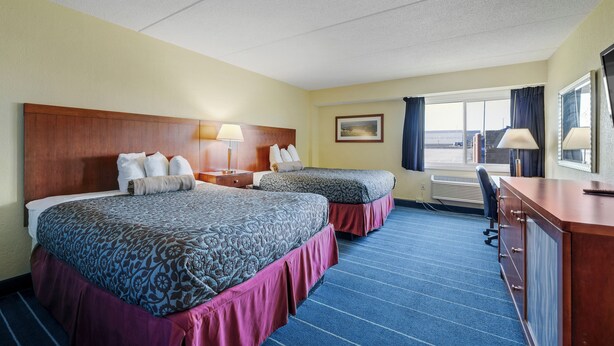 A hotel room with two beds, a desk, and a view of the outdoors.