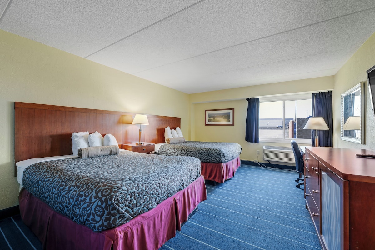 A hotel room with two beds, a desk, and a view of the outdoors.