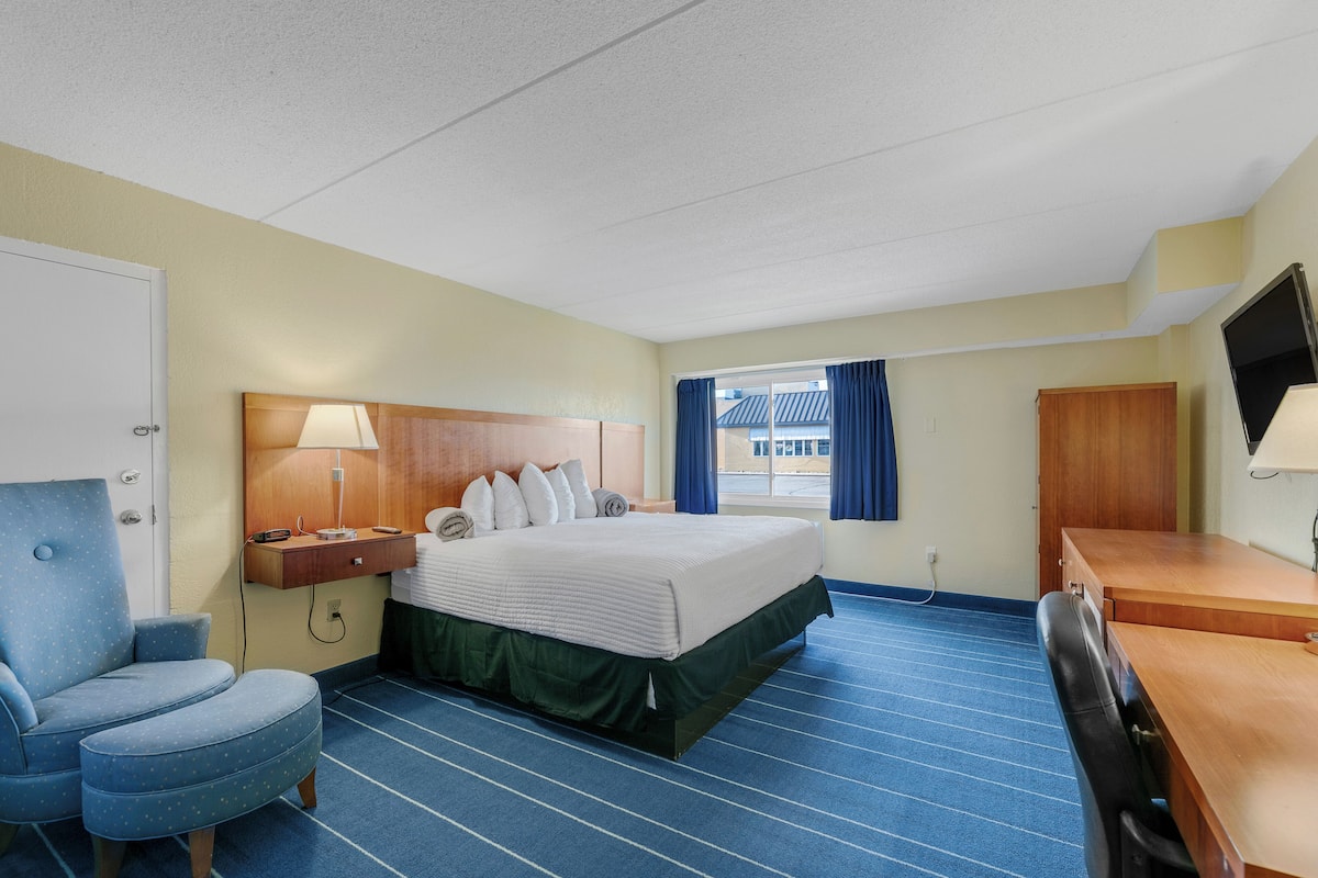 A hotel room with a bed, a desk, a chair, a TV, and a window with curtains.
