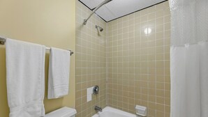 A bathroom with beige tiled walls, a white bathtub, and two white towels hanging on a rack.