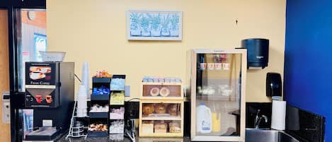 A coffee station with a coffee machine, cups, and a refrigerator with beverages.