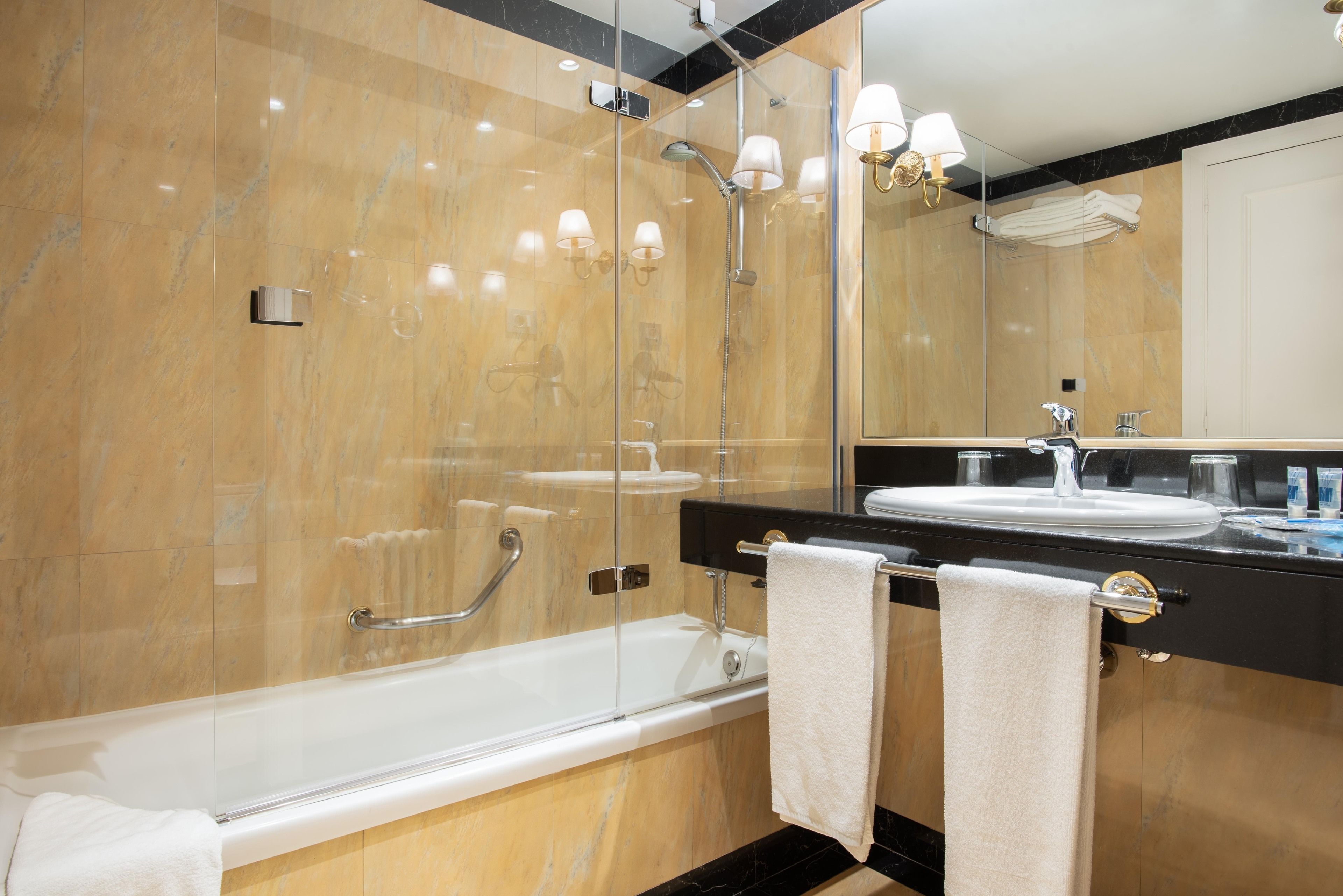 A modern bathroom with a glass-enclosed shower, a black countertop, and a large mirror.