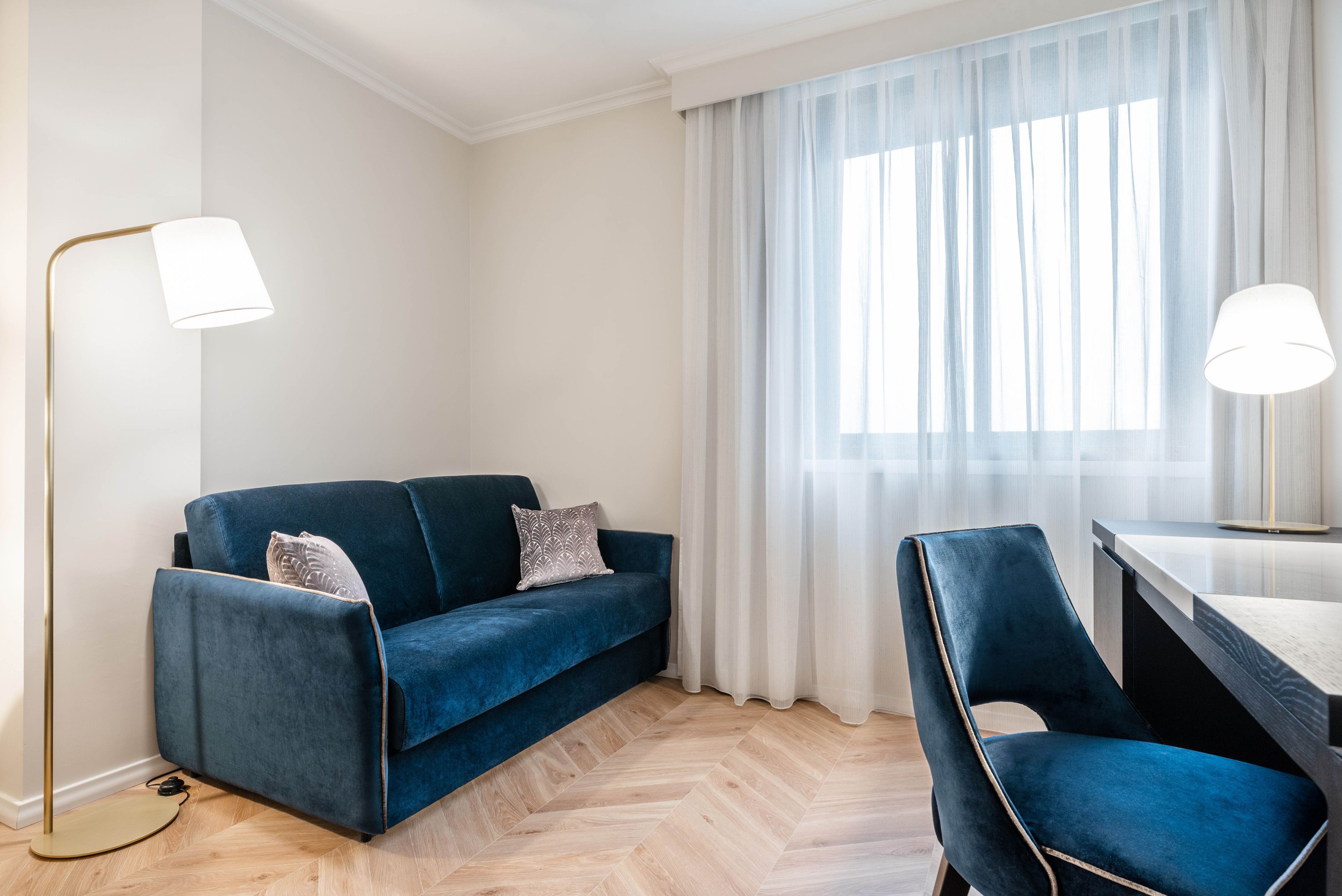 A modern living room with a blue sofa, a matching armchair, a small table, and a floor lamp.