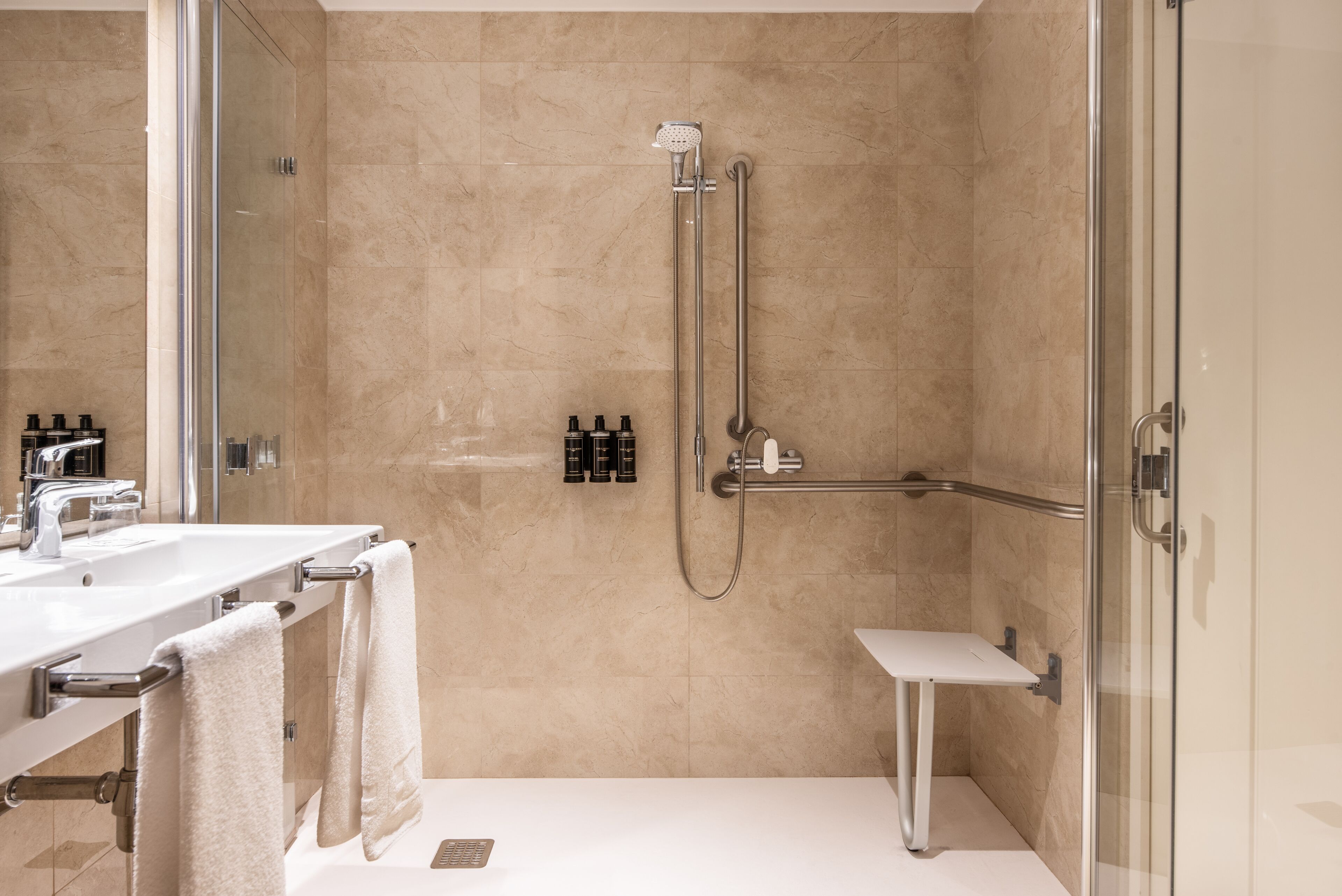 Ein modernes Badezimmer mit einer gläsernen Duschkabine, einem weißen Waschbecken und einem Waschtisch mit Handtüchern.