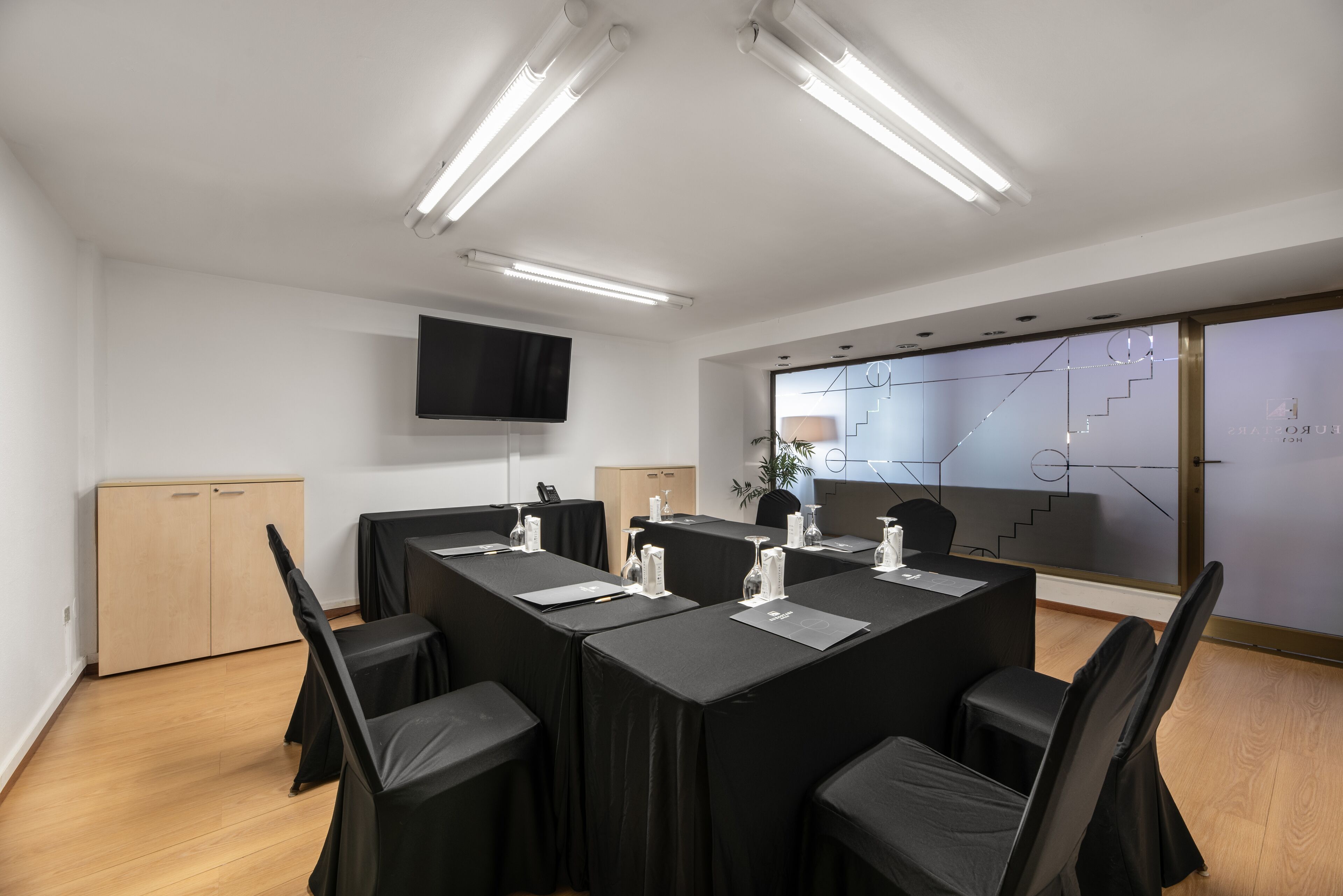 A conference room with a long table, black chairs, and a flat-screen TV on the wall.