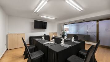 Een vergaderruimte met een lange tafel, zwarte stoelen en een flatscreen aan de muur.