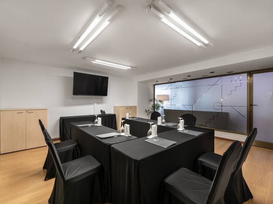 Een vergaderruimte met een lange tafel, zwarte stoelen en een flatscreen aan de muur.