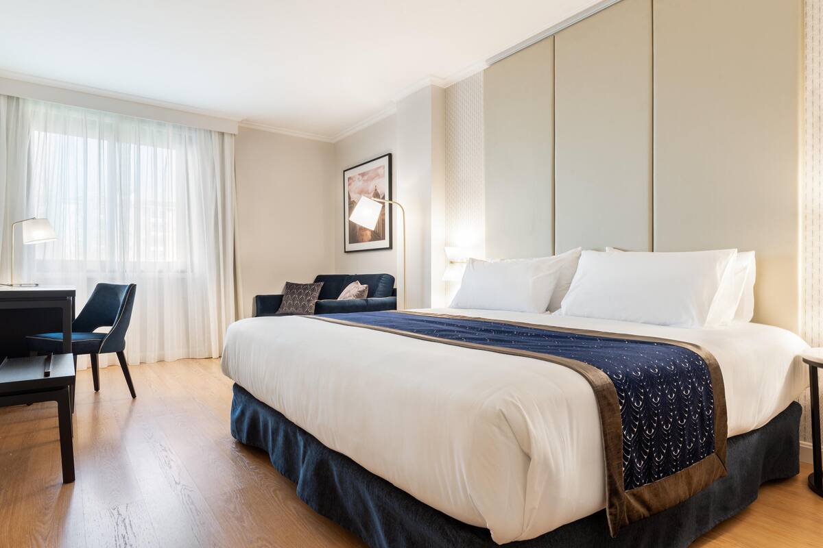 A hotel room with a large bed, a desk, and a chair.