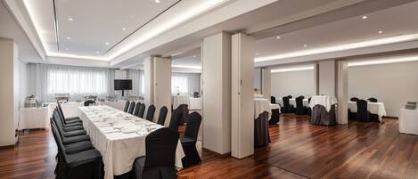 A spacious conference room with a long table, chairs, and a kitchen area in the background.