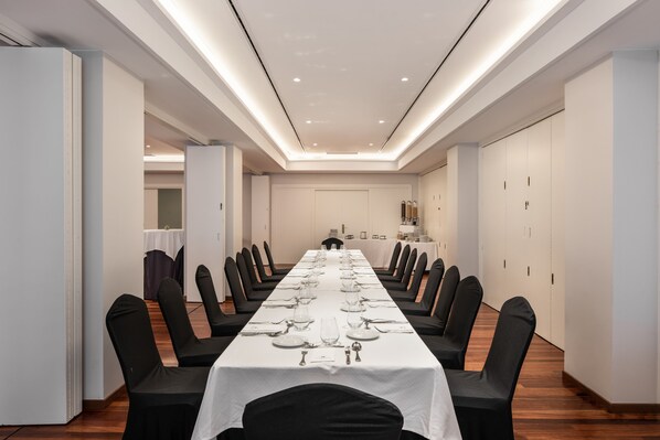 Une salle de conférence avec une longue table préparée pour une réunion, entourée de chaises, avec un plafond et des murs blancs.