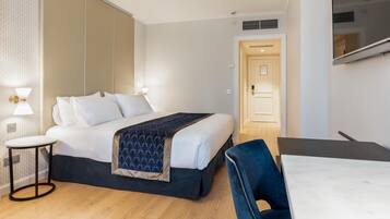 Una habitación de hotel con cama, mesita de noche, silla y televisor montado en la pared.