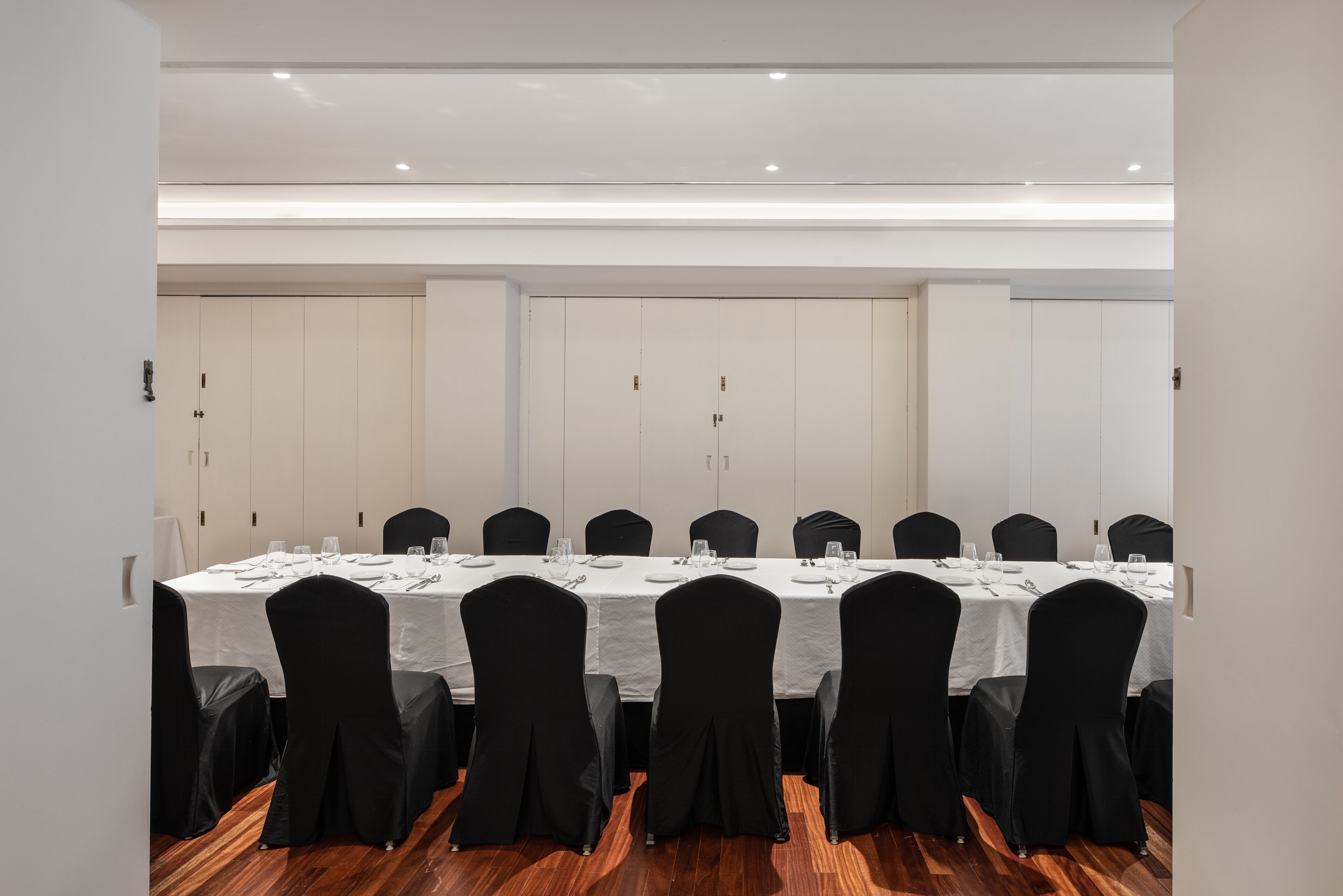 Une salle de conférence avec une longue table, des chaises noires et des nappes blanches.