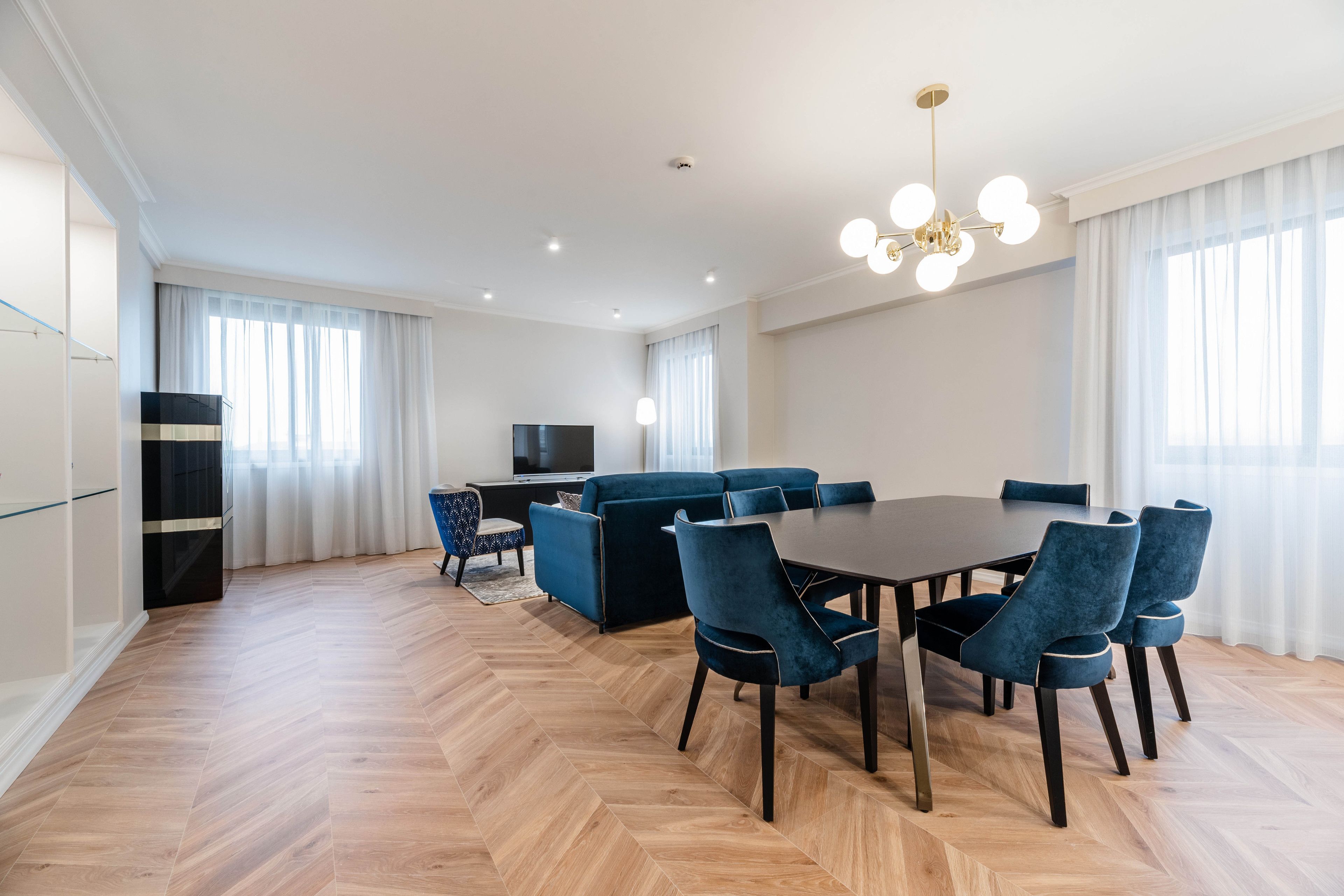 A modern living room with a dark wooden dining table, blue upholstered chairs, a blue sofa, and a television.