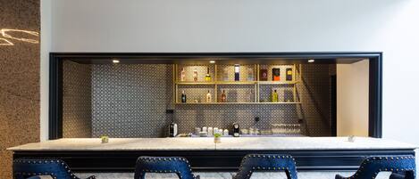 Eine Bar mit einer Marmor-Arbeitsplatte, blau gepolsterten Sesseln und einer gefliesten Rückwand mit Flaschen.