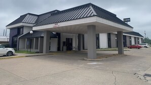A hotel with a covered entrance, a sign indicating a clearance of 12 feet, and a parking lot with several cars. - Mustang Inn (Paducah)
