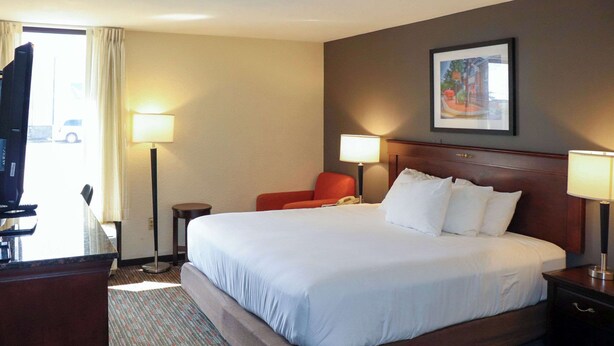 A hotel room with a large bed, two bedside lamps, a chair, a desk, and a TV. - Mustang Inn (Paducah)