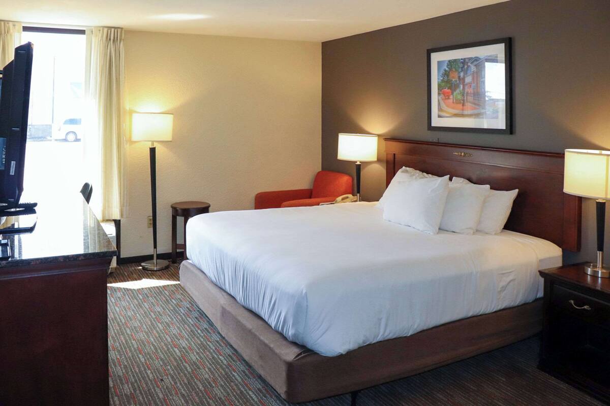 Een hotelkamer met een groot bed, twee bedlampen, een stoel, een bureau en een televisie.