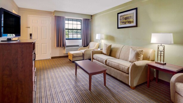 A hotel room with a sofa, two armchairs, a TV, a lamp, and a framed picture on the wall. - Baymont by Wyndham Jacksonville Orange Park (Jacksonville)