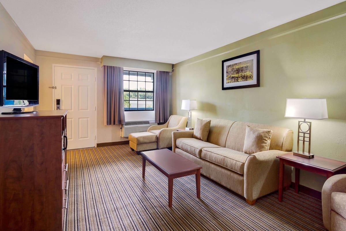 Une chambre d’hôtel avec un canapé, deux fauteuils, une télévision, une lampe et un tableau encadré au mur.