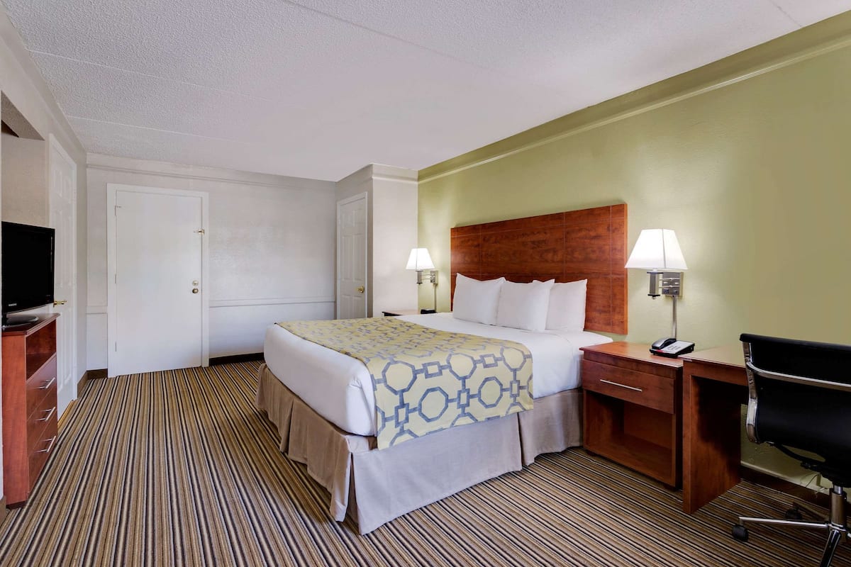 Une chambre d’hôtel comprenant un lit, deux tables de chevet avec des lampes, un bureau avec une chaise et un téléviseur posé sur une commode.