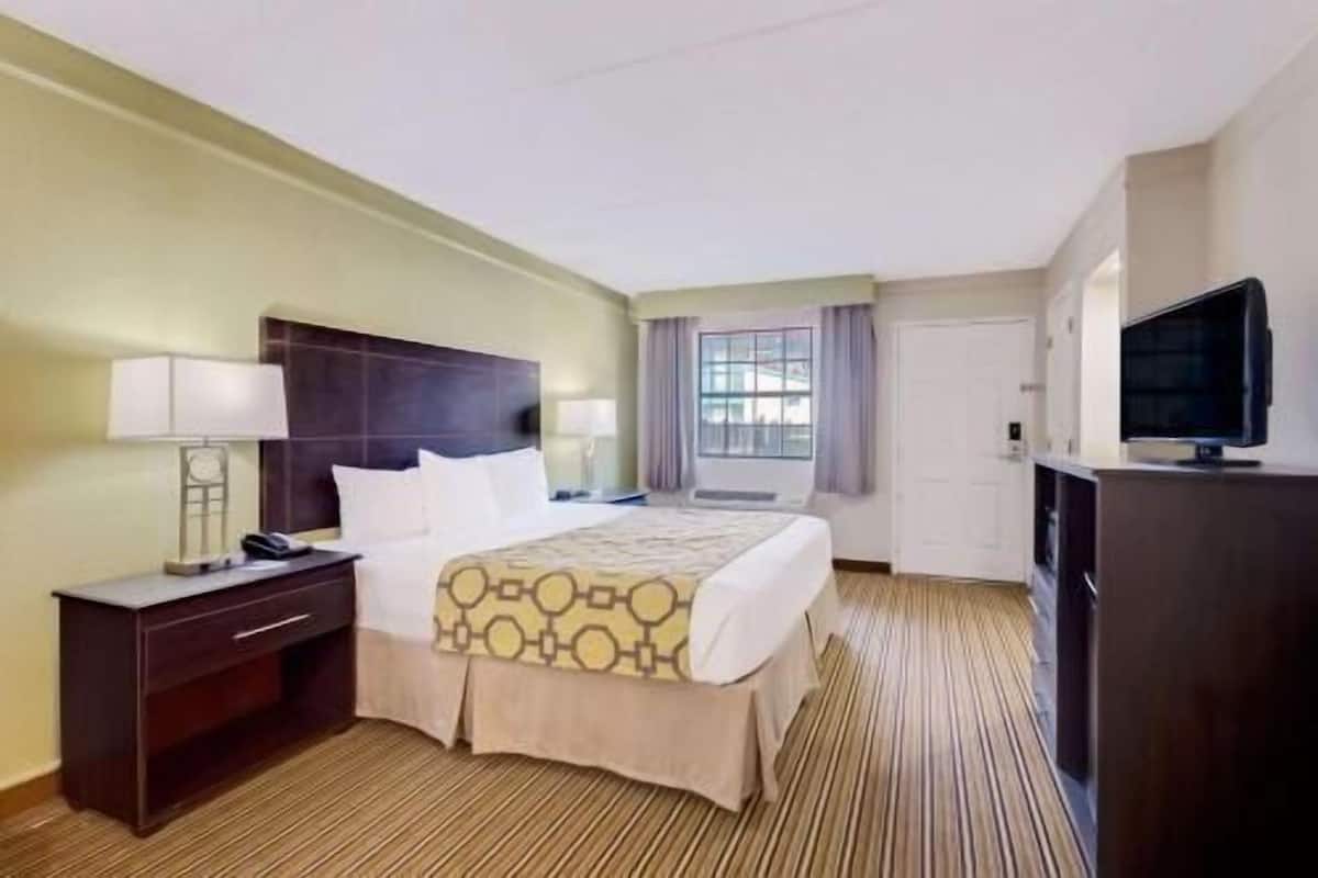 Une chambre d’hôtel avec un lit, une table de chevet, une lampe, une télévision et une fenêtre avec des rideaux.