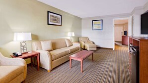 A hotel room with a sofa, armchair, and a television. - Baymont by Wyndham Jacksonville Orange Park (Jacksonville)