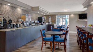 A modern kitchen with a stone backsplash, a coffee station, and a dining area with blue chairs and a long table. - Baymont by Wyndham Jacksonville Orange Park (Jacksonville)